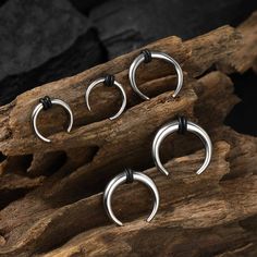 three pairs of silver nose rings sitting on top of a piece of drifty wood