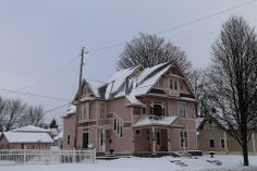 a large pink house with snow on the ground and trees in front of it,