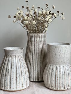 three white vases sitting on top of a table next to each other with flowers in them