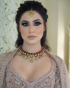 a woman wearing a gold and red choker with jewels on her neck, standing in front of white flowers