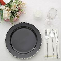 a black plate and silverware on a white table cloth with flowers in the background