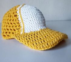 a crocheted yellow and white baseball cap on a table with a white wall in the background