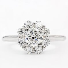 an engagement ring with a large diamond surrounded by smaller round brilliant cut diamonds in white gold