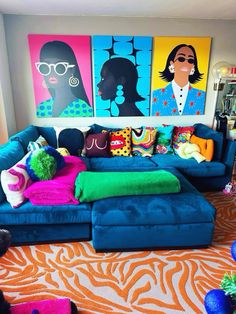 a living room filled with blue couches covered in pillows and colorful paintings on the wall