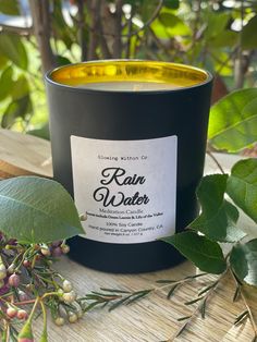 a candle sitting on top of a wooden table next to leaves and berries with the label rain water