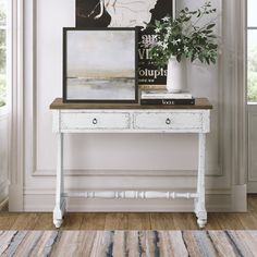 a white table with two drawers and a painting on top of it next to a window