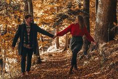 a man and woman holding hands while walking through the woods on a trail in autumn