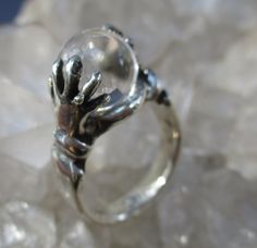 "This is a Hand Cast Sterling Silver Ring with a unique \"Crystal Ball\" design. It is set with a 10 mm Natural Quartz Crystal Ball. This original design has two hands holding the crystal ball. Unique ring, surely will be noticed everywhere you go. The ring is about 7/16 inch wide on top and tapers to a plain shank in the back. It is 7/16 inch tall. Truly Magical ! This ring is made in a size 7 1/4. I will wrap the ring in a gift box and mail in a small box within 1-2 days of purchase, usually o Mystical Sterling Silver Crystal Ring, Spiritual Sterling Silver Crystal Ring For Formal Events, Spiritual Sterling Silver Crystal Ring For Formal Occasions, Formal Clear Jewelry With Polished Finish, Unique Jewelry With Polished Round Stone Finish, Unique Clear Rings, Unique Clear Round Rings, Mystical Clear Jewelry For Gifts, Oval Sterling Silver Clear Jewelry