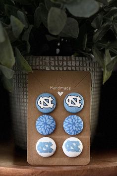 two blue and white earrings sitting on top of a wooden table next to a potted plant