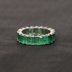 an emerald colored ring sitting on top of a black surface with white diamonds in the middle