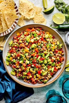 a bowl filled with mexican salad next to tortilla chips and avocado