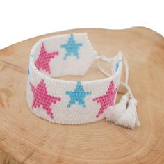 a white bracelet with pink and blue stars on it sitting on top of a wooden table