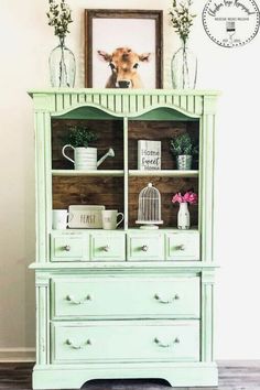 an old china cabinet painted green with white trim and flowers in vases on top