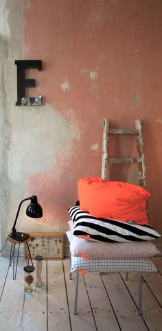 a chair and some pillows in a room with peeling paint on the walls, an old ladder leaning against the wall