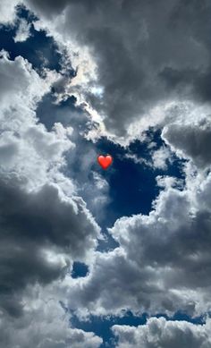 a heart shaped balloon floating in the air on a cloudy day with blue sky and white clouds