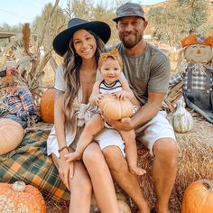 a man and woman sitting on hay with pumpkins