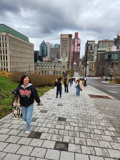 a woman walking down a brick sidewalk in front of tall buildings