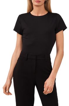 a woman is wearing a black top and pants with her hands in her pockets,