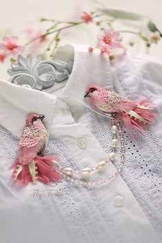 two pink birds are sitting on the collar of a white shirt with pearls and beads