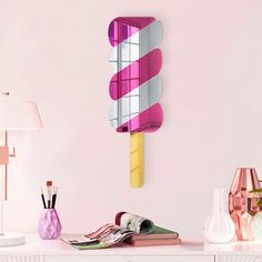 a pink and yellow mirror on the wall above a white dresser with various items in front of it