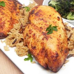 two pieces of chicken on a plate with rice and broccoli next to it