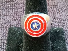 a captain america ring sitting on top of a black piece of cloth with a white star in the center