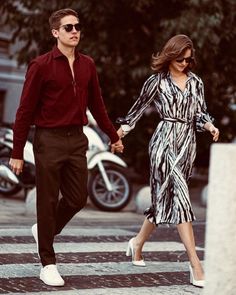 a man and woman walking across a street holding hands