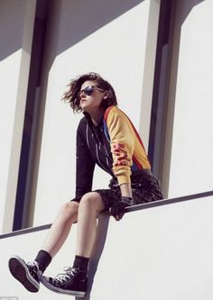 a woman sitting on top of a metal rail next to a building and wearing sunglasses