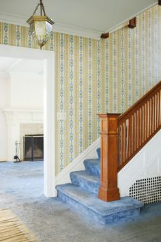 an empty room with blue carpet and wallpaper on the walls, stairs leading up to a fire place