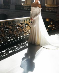 a woman in a white wedding dress standing on a balcony with her hands behind her back