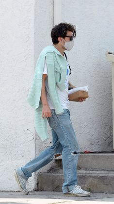 a man walking down the street wearing a face mask and holding a box in his hand