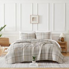 a bed in a room with white walls and wooden flooring next to a potted plant