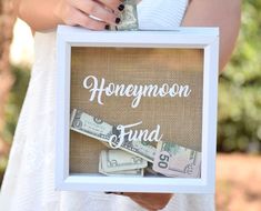 a person holding a frame with money and the words honeymoon fund written on it