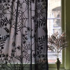 a vase with flowers in it sitting next to a window sill near a spider web curtain