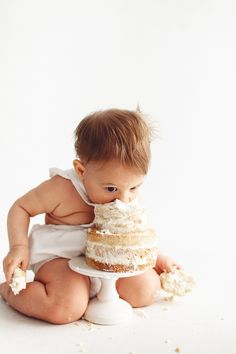 a baby sitting on the floor with a cake in its mouth and looking at it