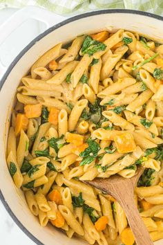 pasta with spinach and carrots in a skillet on the stove top next to a wooden spoon