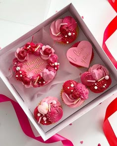 cupcakes with pink frosting and hearts in a box on a white table