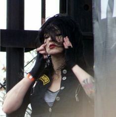 a woman with black hair and piercings is talking on her cell phone while standing in front of a gate