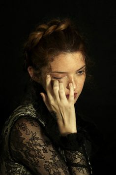 a woman with her hand on her face looking at the camera while wearing a black lace top