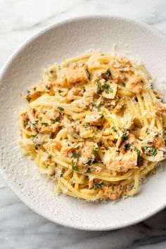 a white bowl filled with pasta covered in parmesan cheese and herbs on top of a marble table