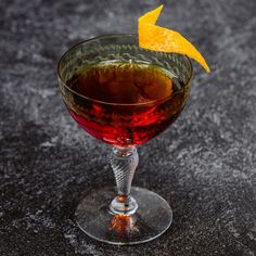 a close up of a drink in a wine glass with an orange peel on top