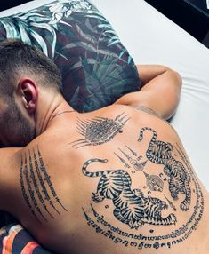 a man laying on top of a bed with tattoos on his back and chest next to a pillow