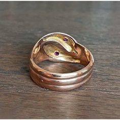 In the quiet, storied streets of Birmingham, 1918—a city teeming with industrious spirit and the echoes of a bygone era—a master goldsmith crafted this splendid creation. With its serpentine elegance, this ring features two serpents entwined in a dance of eternal allure. Each snake, rendered in lustrous 9 karat gold, showcases the hallmark of an era: the anchor for Birmingham and the letter 'T' denoting the year 1918, alongside the revered maker’s mark ‘H.W. Ld’. These symbols of authenticity promise not just a piece of jewelry, but a journey through time.  Adorning each serpent's head is a resplendent fuchsia-colored round faceted ruby measuring 2.6 mm across. These radiant gemstones capture the essence of a captivating twilight and reflect a world where opulence meets the extraordinary. Antique Hand Forged Rings For Formal Occasion, Antique Hallmarked Snake Ring, Antique 14k Gold Hand Forged Rings, Vintage Hand Forged Yellow Gold Rings, Elegant Hallmarked Snake Ring, Heirloom Hallmarked Snake Ring As Gift, Vintage 14k Gold Snake Ring, Vintage Yellow Gold Snake Ring As Gift, Vintage 14k Gold Snake Ring As A Gift