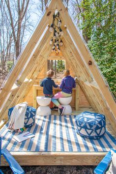 two people sitting on stools in front of a small wooden structure that is built into the ground