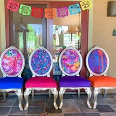 there are four chairs that have been painted with different colors and designs on them, sitting in front of a glass door