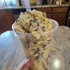 a person holding up a plastic cup filled with ice cream and chocolate chip cookies on top