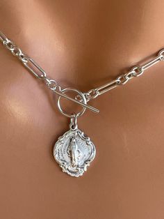 "This is a stunning thick, solid 925 sterling silver choker necklace with a unique Virgin Mary medallion that hangs from toggle clasp in front. This gorgeous Mother Mary charm measures 19x15mm and has the Miraculous Mary stamp with cross heart and stars on backside.. Made here is the USA by skilled silversmiths this pendant is absolutely incredible. This lovey sterling silver chunky chain links measure 8x4mm and 4mm, 3-1 pattern. Model is wearing a 15\" choker length. Comes in a gift box, ready Etsy Necklaces Unique, Silver Engraved Lariat Jewelry, Sterling Silver Choker With Lobster Clasp, Silver Link Necklace With Charms, Silver Link Necklaces With Charms, Engraved Silver Lariat Jewelry, Sterling Silver Necklace With Toggle Clasp As Gift, Silver Toggle Choker Necklace With Lobster Clasp, Elegant Medallion Jewelry With Toggle Clasp