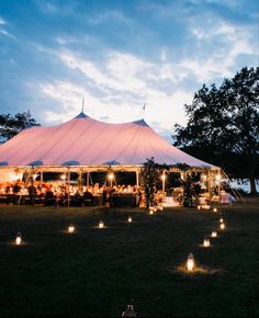 a large tent with candles lit up in front of it and people sitting at the tables