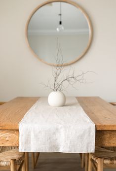 a white vase sitting on top of a wooden table next to a mirror and chair