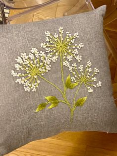 a gray pillow with white flowers on it sitting on a wooden floor next to a glass vase